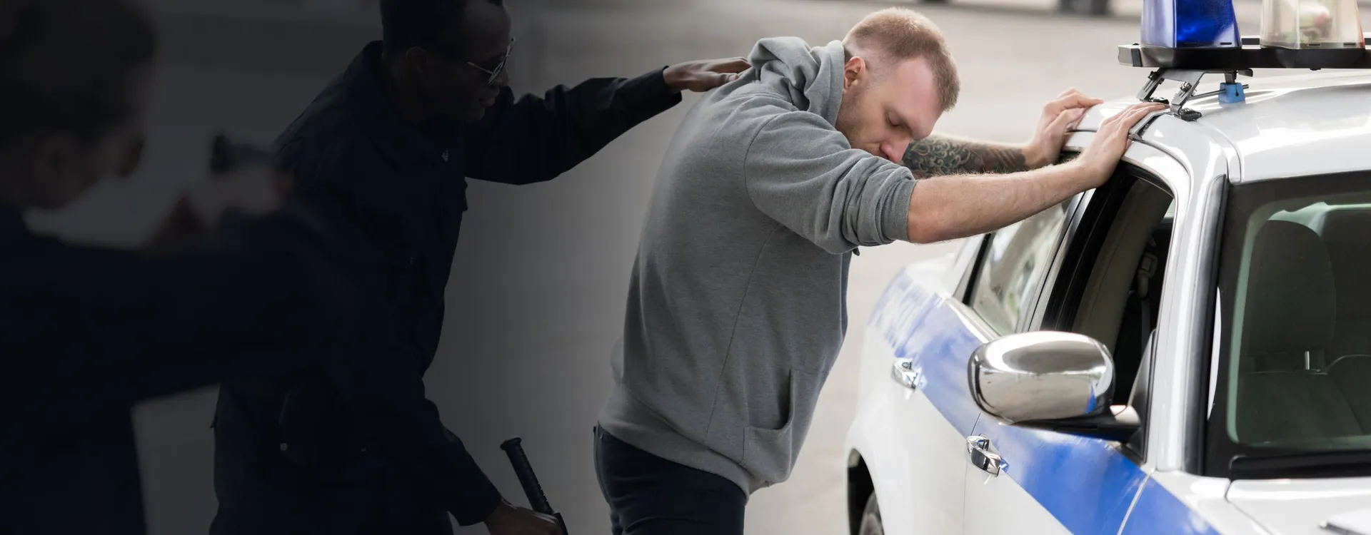 Officers pushing a man against a patrol car while another officer stands by